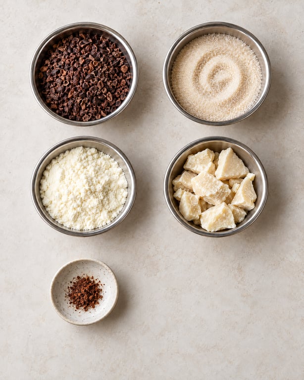 Bowls of cacao nibs, sugar, milk powder, irregular cocoa butter chunks and spice