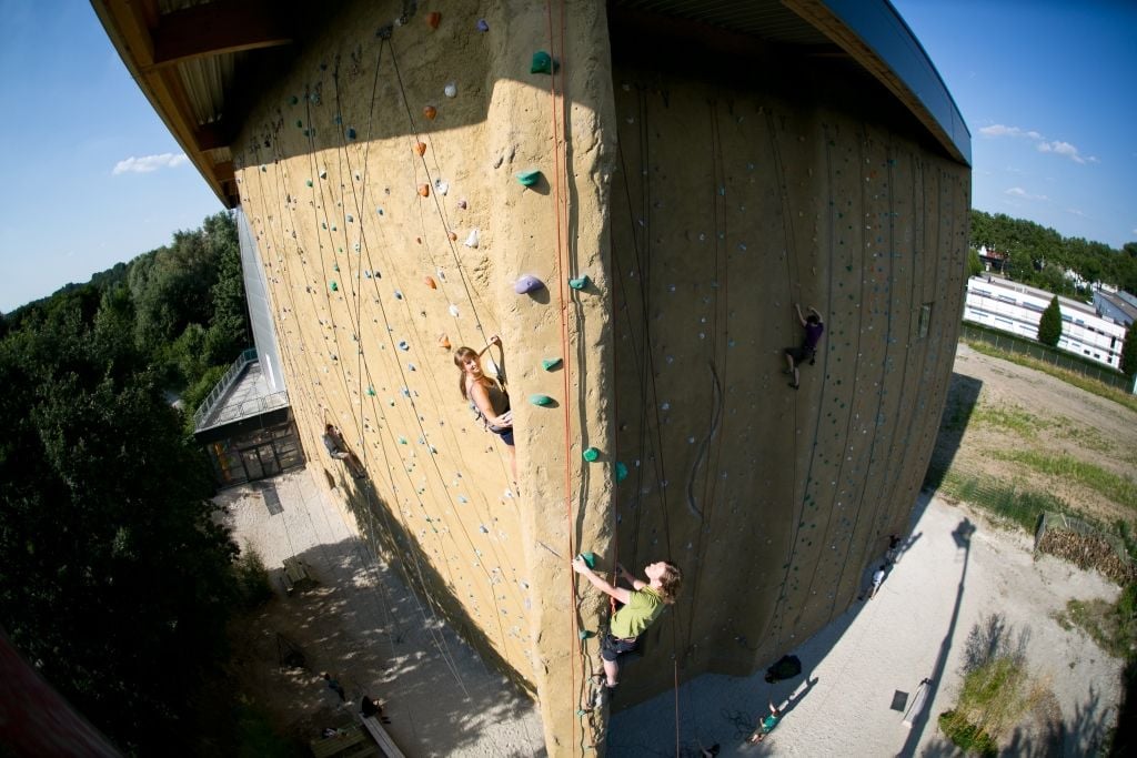 Zwei Personen klettern an einer großen Kletterwand im freien hoch