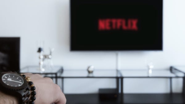 Person liest ein Buch, währenddessen Netflix auf dem Fernseher läuft
