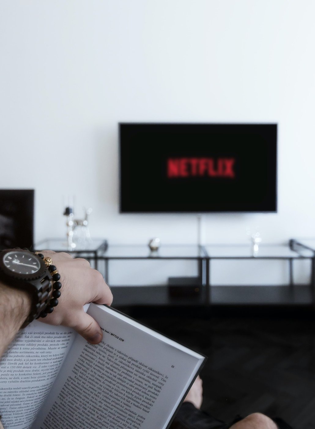 Person liest ein Buch, währenddessen Netflix auf dem Fernseher läuft