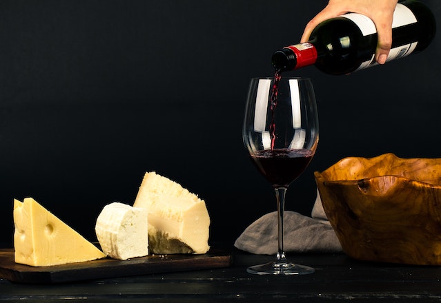 Neben verschiedenen Stücken Käse wird ein Rotwein eingegossen. 
