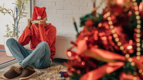 mann sitzt mit heruntergezogener weihnachtsmütze an heilig abend neben einem weihnachtsbaum