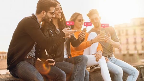 Vier Menschen sitzen amüsiert zusammen und beschäftigen sich mit Instagram auf ihren Handys.
