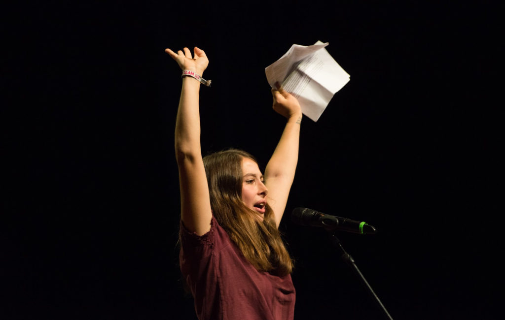 Eine Poetry Slammerin reißt auf der Bühne ihre Arme hoch