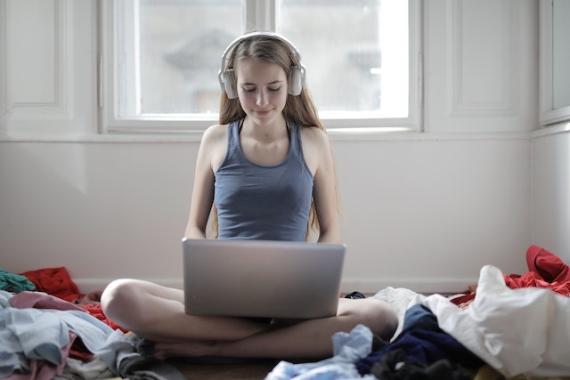 Eine Frau sitzt mit Kopfhörern vor ihrem Laptop auf dem Bett