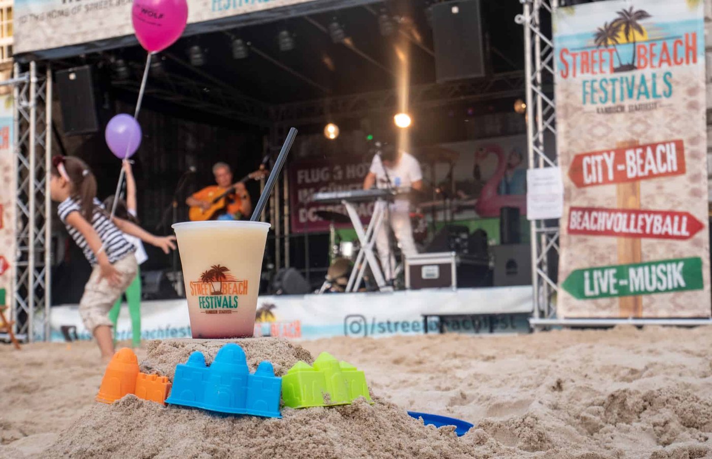 Auf einer Sandfläche stehen auf einem kleinen Sandhügel Sandförmchen und ein Getränkebecher als Symbolbild für Gourmet Festivals