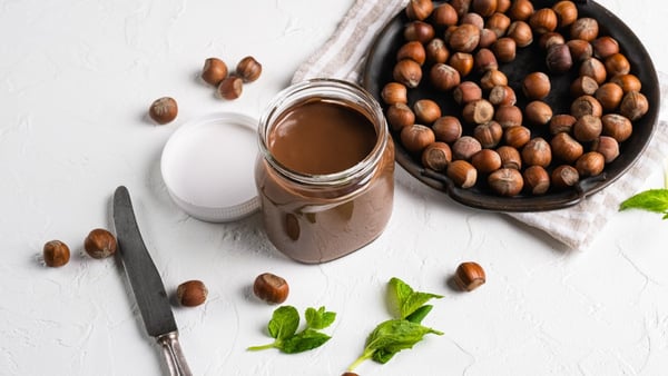 Ein Glas Nutella und mehrere Haselnüsse auf einem Tisch