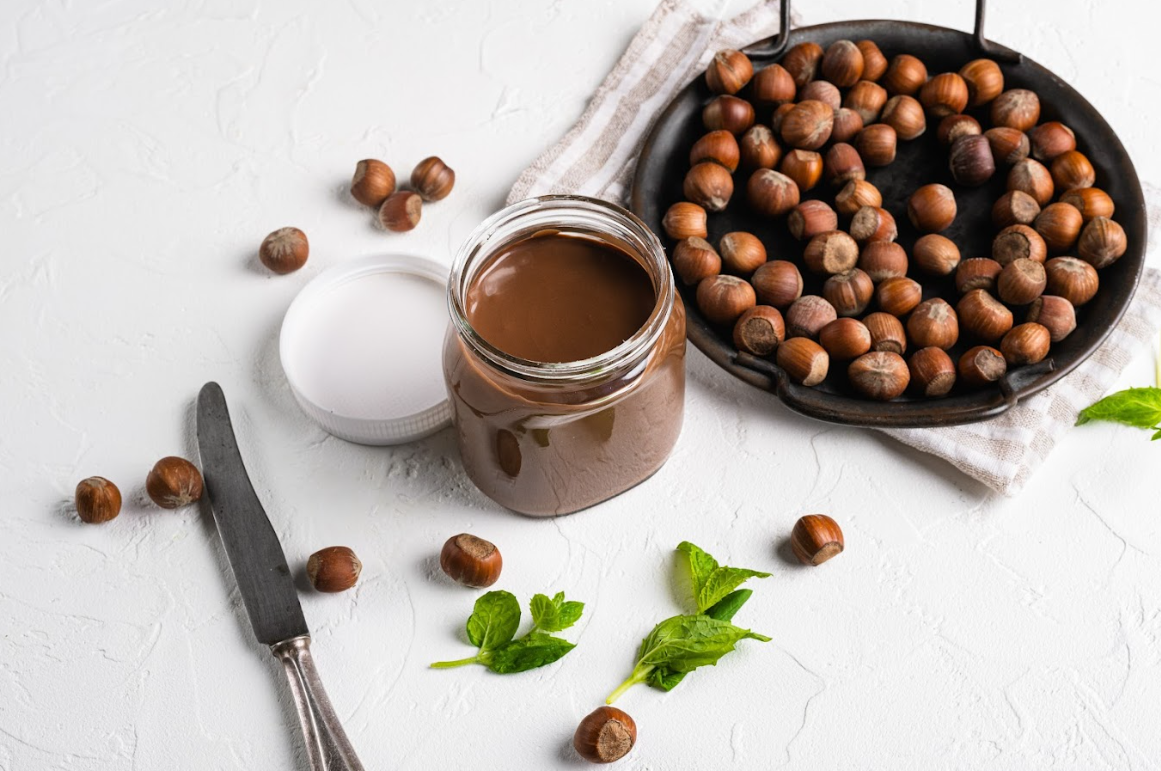Ein Glas Nutella und mehrere Haselnüsse auf einem Tisch