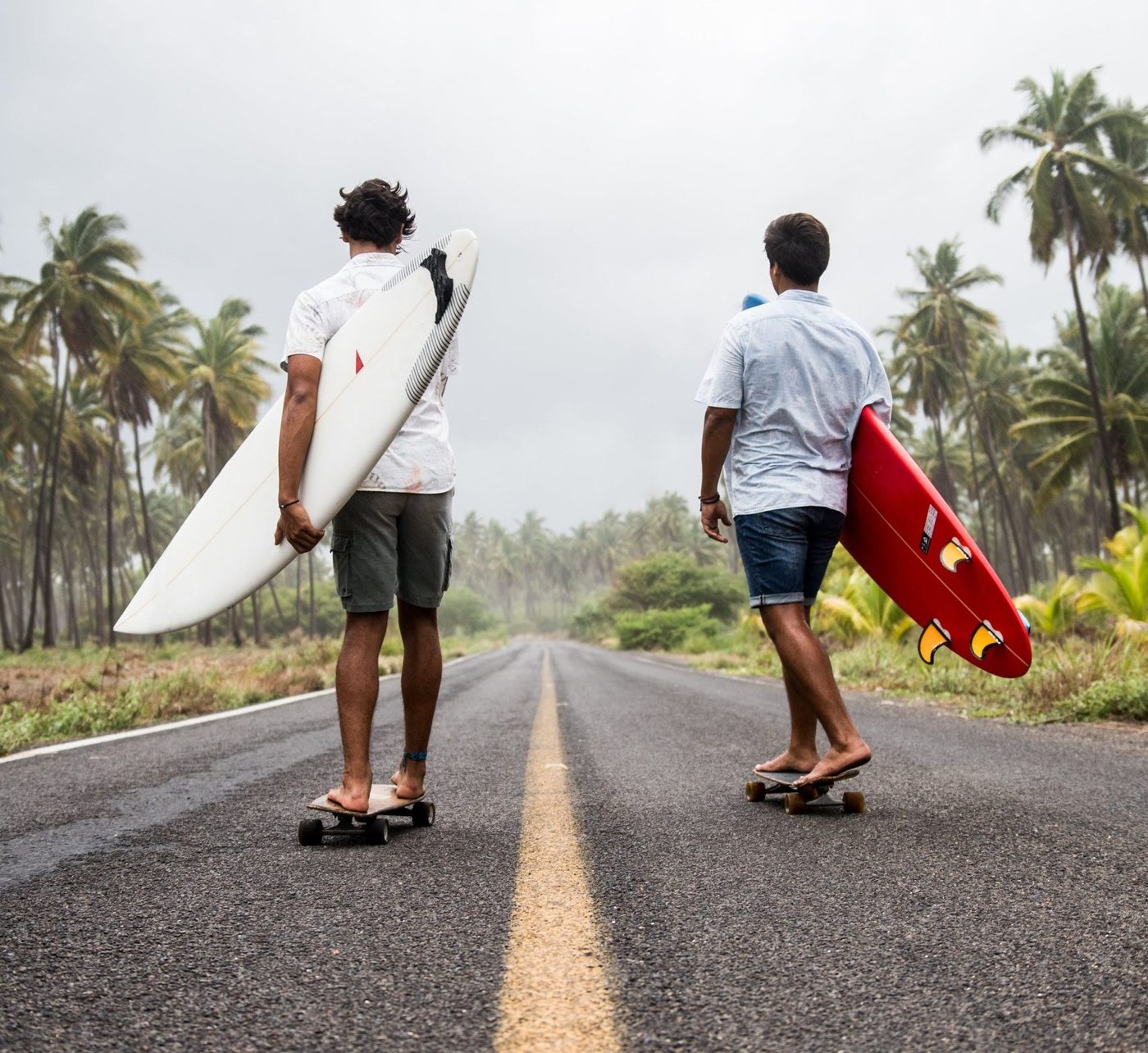 Zwei Personen mit Surfbrettern unter dem Arm skaten eine Straße entlang