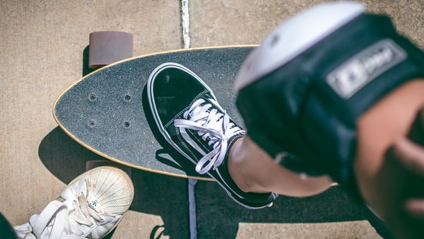 Person mit Knieschoner stellt ein Bein auf ein Skateboard