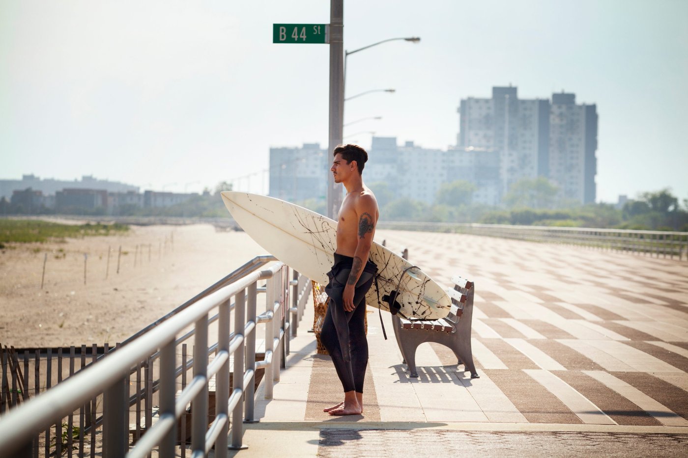 Mann mit einem Surfbrett steht am Strand und guckt aufs Wasser