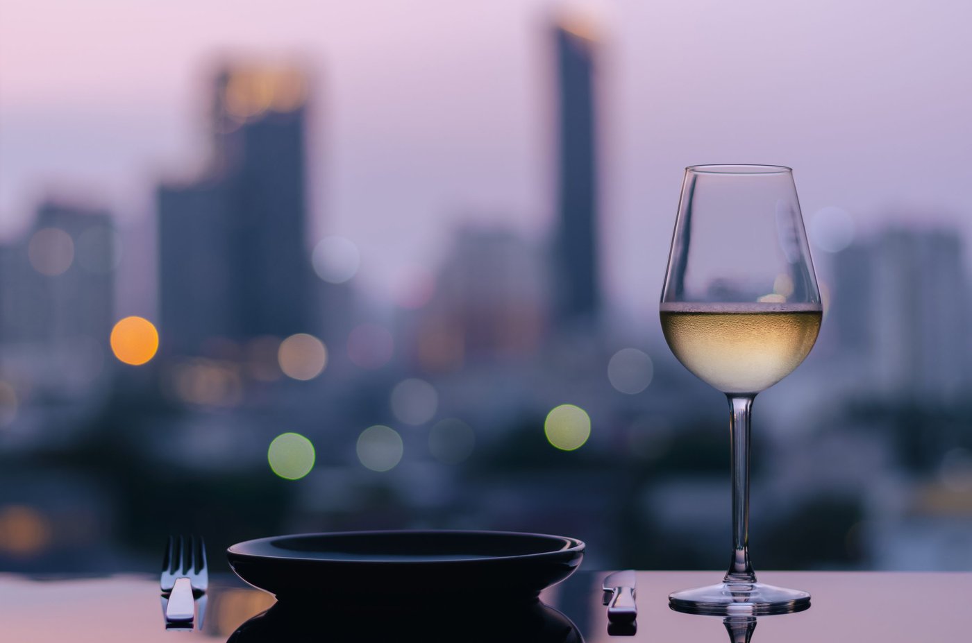 Ein Weinglas in einer Rooftop-Bar, im Hintergrund ist die Skyline einer Stadt zu sehen