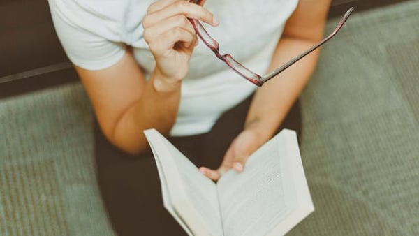 ein Mann liest ein Buch und hält dabei seine Brille in der Hand