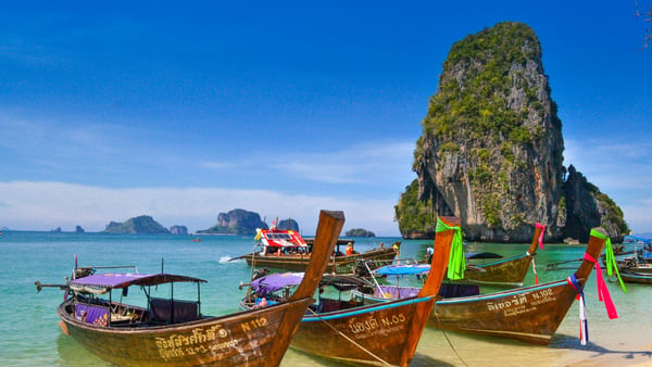 Traditionelle Longtail-Boote an einem tropischen Strand in Südthailand mit türkisfarbenem Meer und Kalksteinfelsen