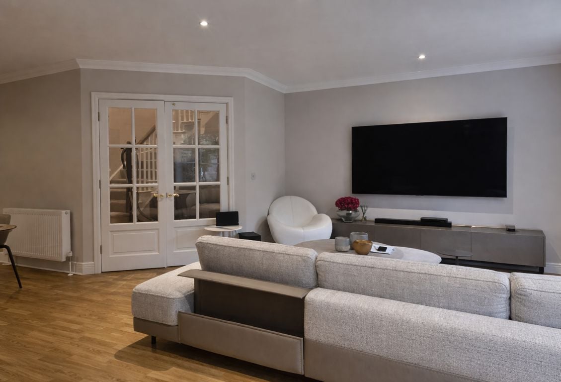Contemporary living room with a gray sectional, white chair, and wall-mounted TV.