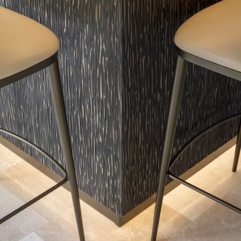 Close-up of two barstools against a textured wall with a modern design.