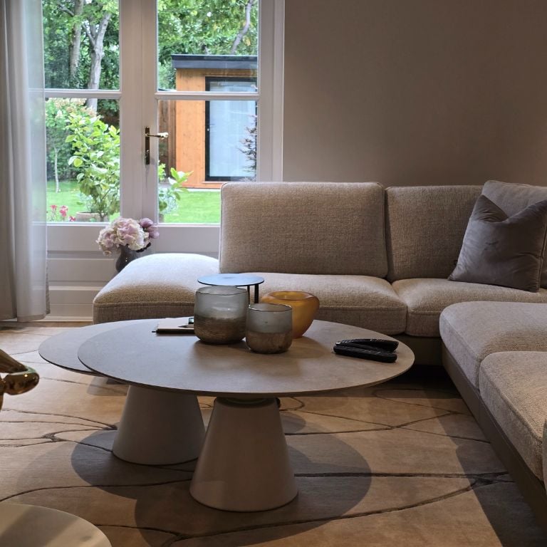 Living room with plush sofa, coffee table, and scenic garden view through the windows.
