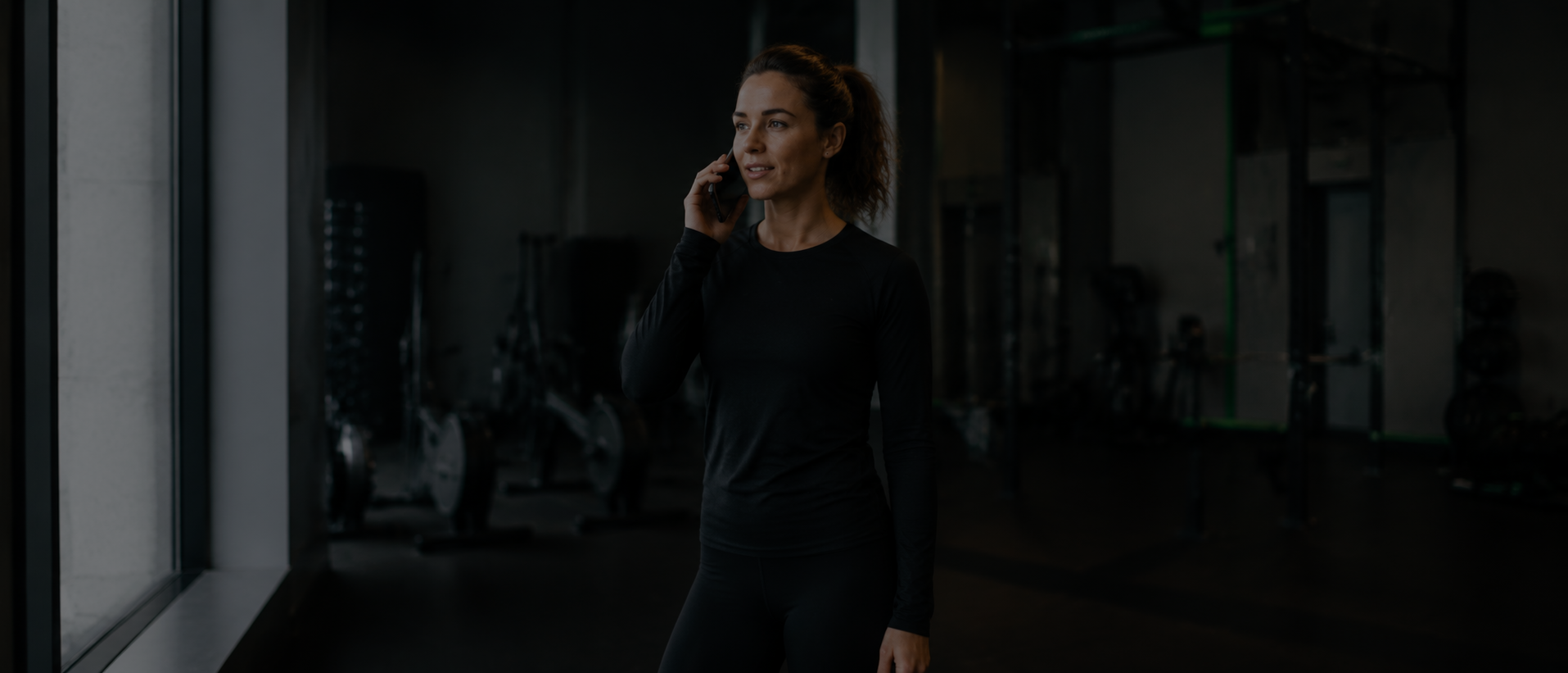 Moteris sporto salėje kalba telefonu prieš pirmą konsultaciją su asmeniniu treneriu