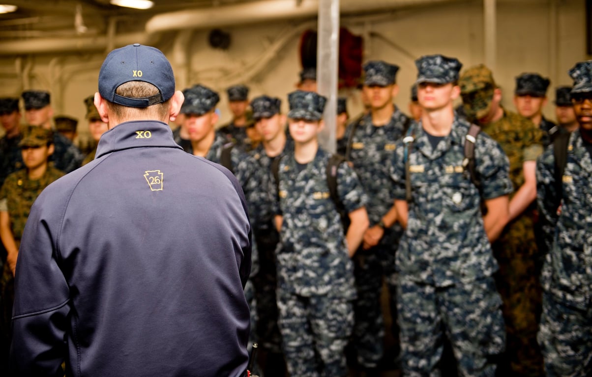 A ship's executive officer briefs a group of uniformed NROTC midshipmen aboard a Navy ship during a summer cruise