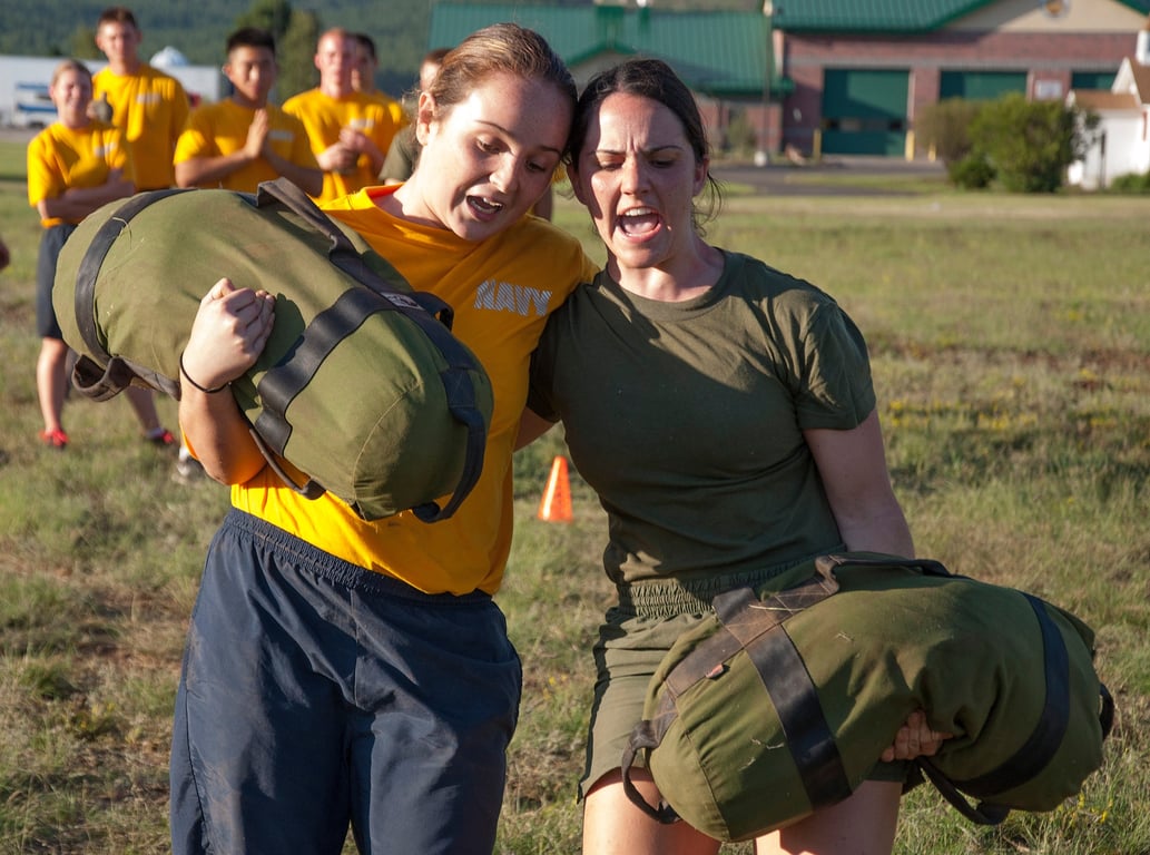 Two NROTC midshipmen in Navy physical-training gear carry sandbags during an outdoor orientation fitness exercise