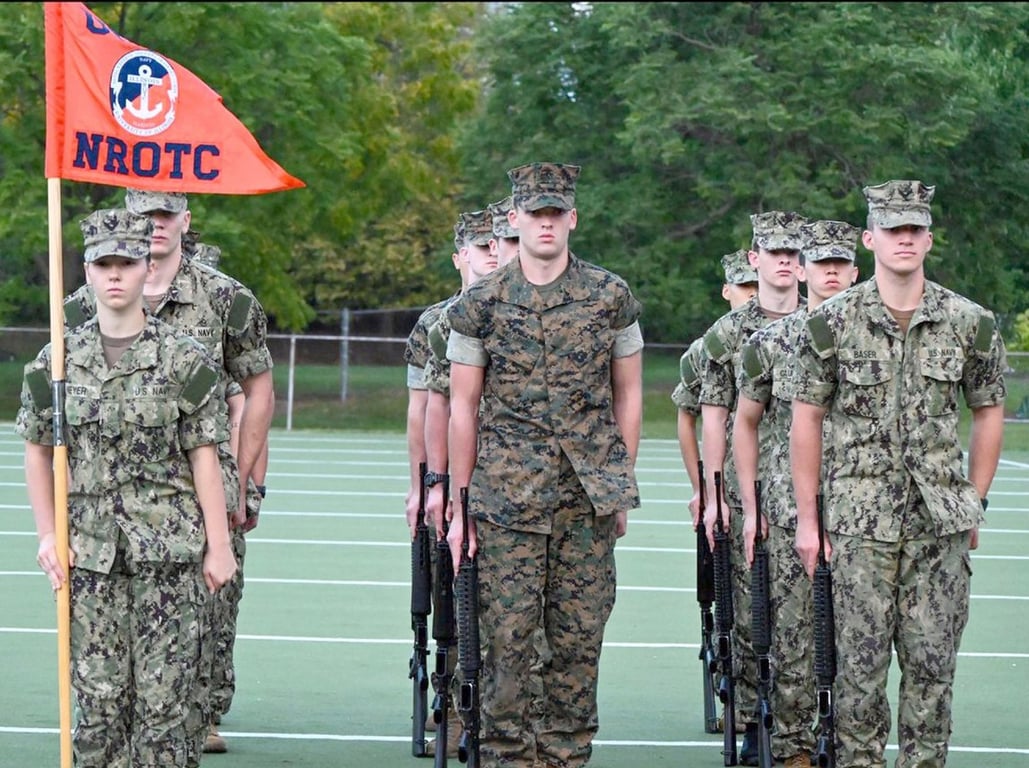 A university NROTC color guard stands in formation with the unit guidon and rifles at an intercollegiate drill competition