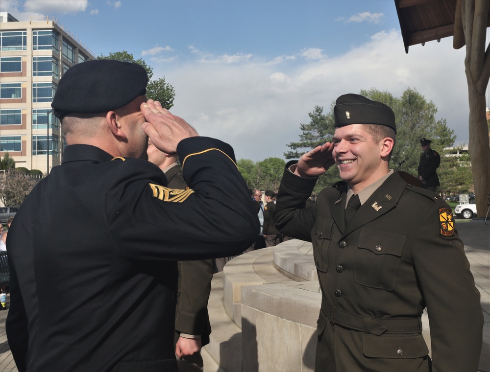 A senior Army noncommissioned officer renders the first salute to his son, a newly commissioned second lieutenant, at an outdoor ROTC commissioning ceremony.