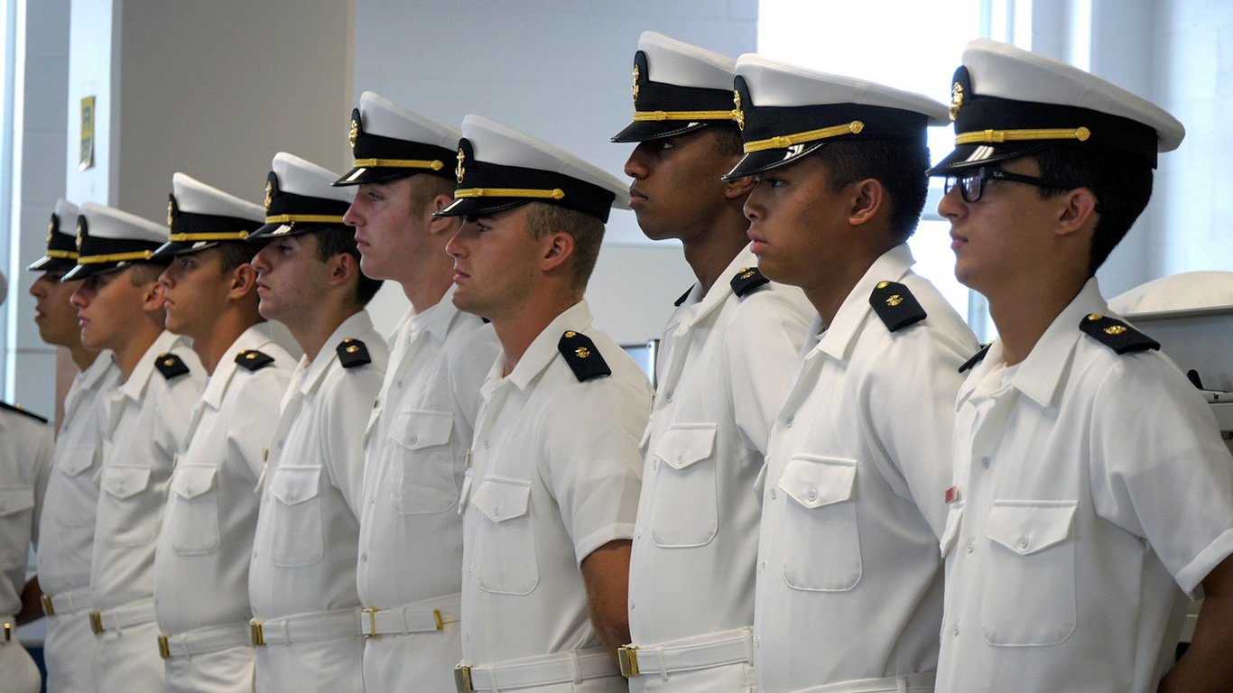 A line of Navy ROTC midshipmen in summer dress white uniforms standing for a uniform inspection