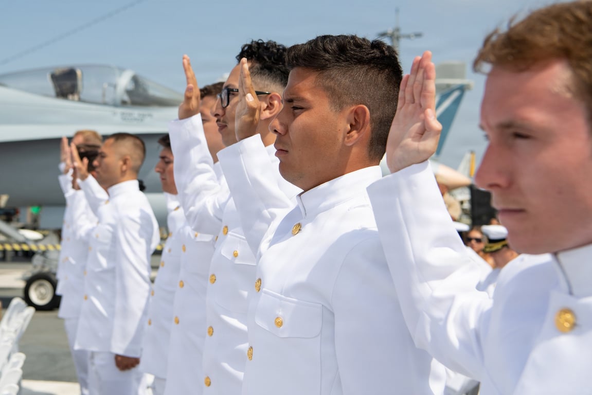 NROTC graduates in dress whites take the oath of office at a commissioning ceremony aboard the USS Midway Museum