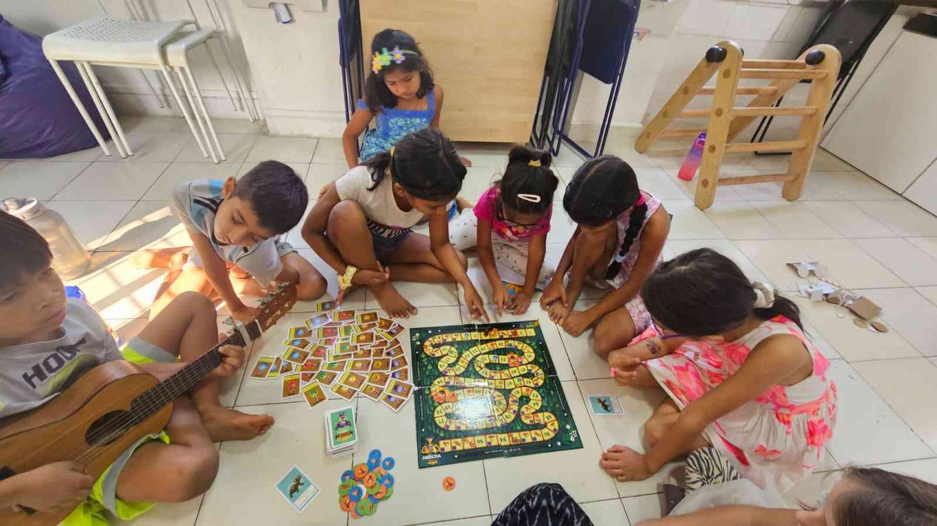 Kids playing a board game while another serenades them with his guitar