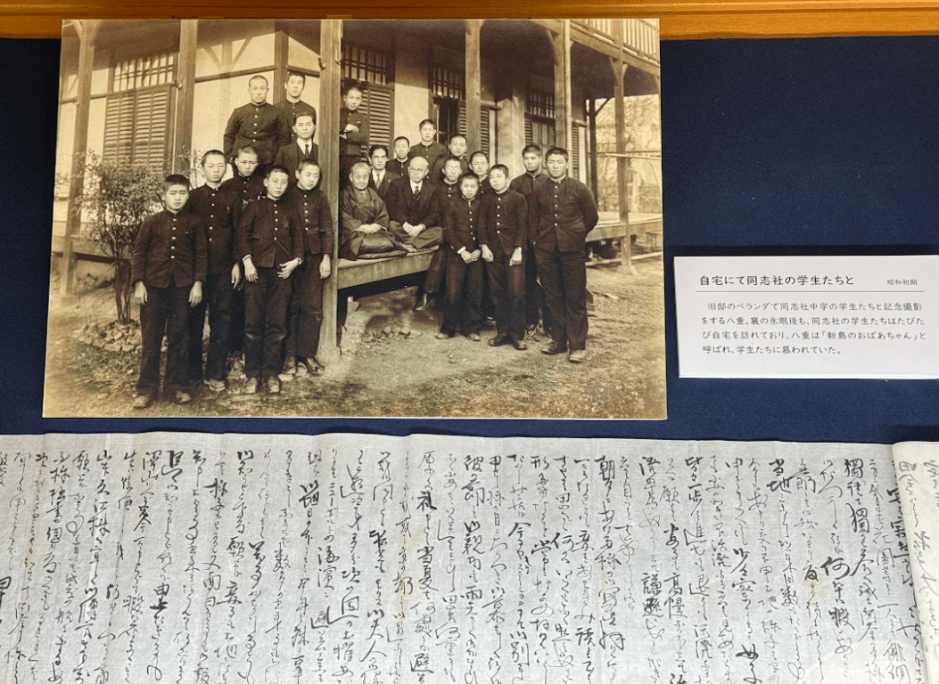 在舊邸的陽台上，八重與同志社中學的學生們合影紀念。在新島襄辭世之後，同志社的學生們依然多次拜訪她的住所。八重被學生們親切地稱為「新島奶奶（新島のおばあちゃん）」。