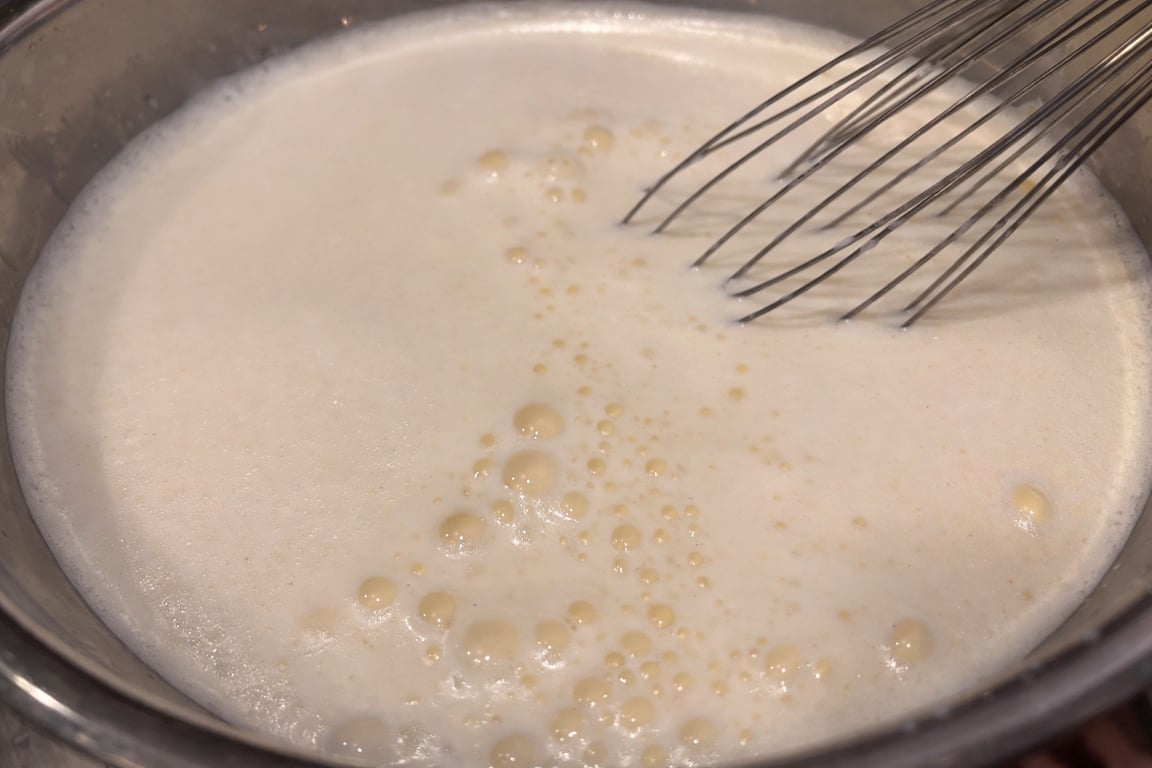 Slowly whisk the hot milk into the egg yolks to temper them, warming the eggs gently without scrambling.