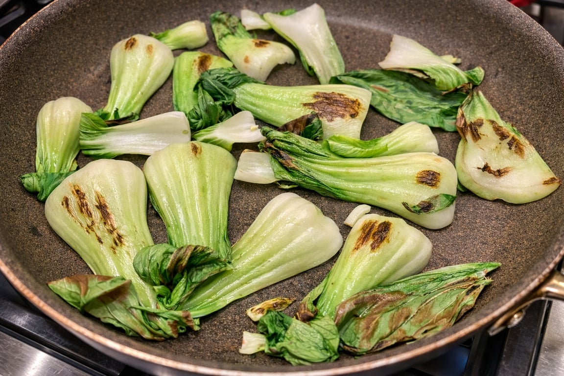 Baby bok choy browning in a very hot, dry pan. Light caramelization, not hard char.