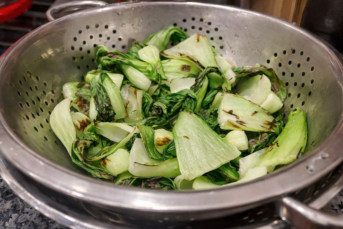 Charred baby bok choy resting in a colander to drain.