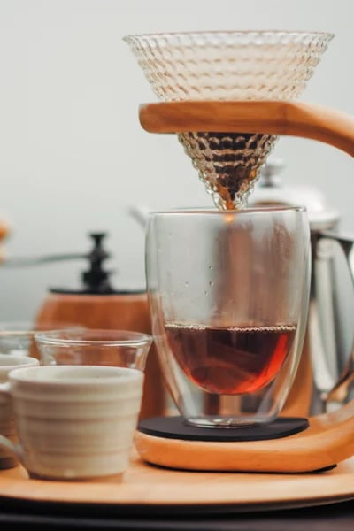 A glass pour-over brewer on a stand dripping into a glass cup, with a ceramic cup placed alongside — the visual foundation of the Pillar & Press methodology