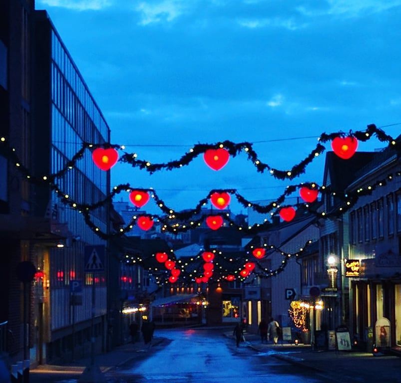 Tromsø, Norway - middle of the afternoon in December. Called the Paris of the north. Showing a quiet street with hanging red heart lights strung between buildings.