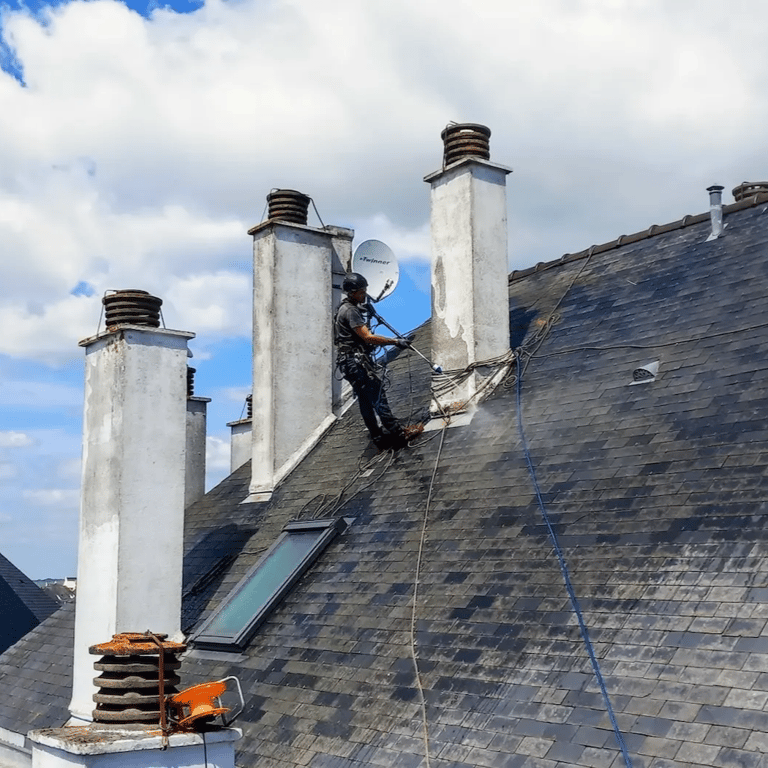 Un technicien cordiste en équipement de sécurité nettoie les tuiles du toit d'un bâtiment historique.