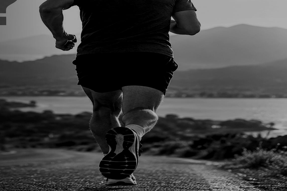 Coureur vu de dos en mouvement, cadrage resserré sur la foulée, dans une photographie sombre en noir et blanc.