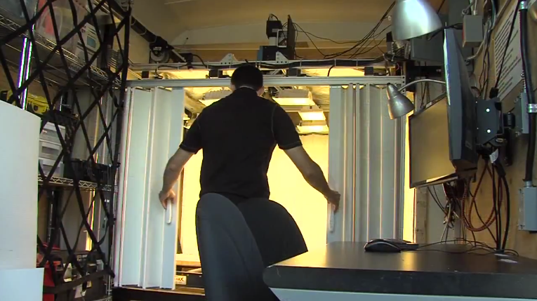 View of the inside of the Core Mapper mobile imaging lab. A man in a short sleeve shirt is opening sliding blinds to visually inspect the scanning area and make sure the boxes of rock samples are centred.