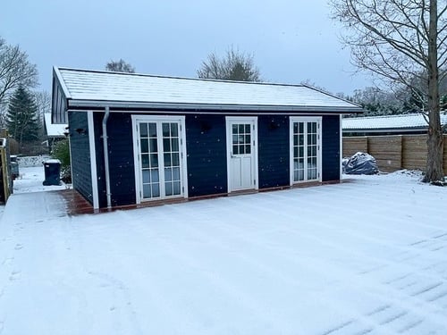 Dark-colored annex building with white doors and trim, surrounded by snow in a winter scene. Screw piles are a great garden room foundation.