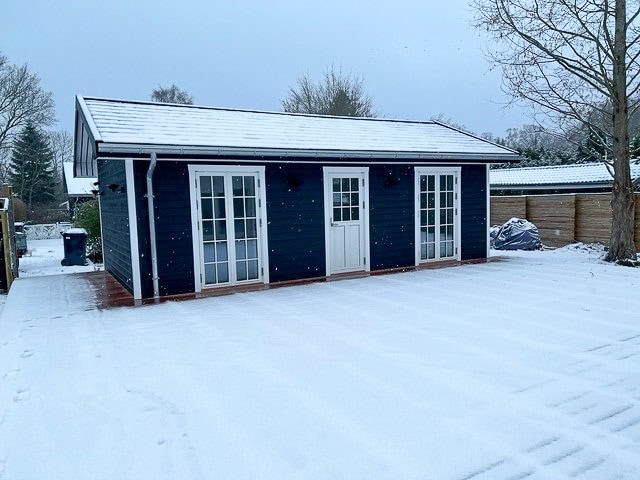 Dark-colored annex building with white doors and trim, surrounded by snow in a winter scene. Screw piles are a great garden room foundation.
