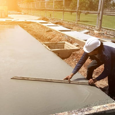 Person finishing wet concrete using a screeding tool on an outdoor construction project under bright sunlight.