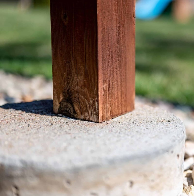 Detail shot showing the base of a wooden deck post supported by a rough concrete footing.