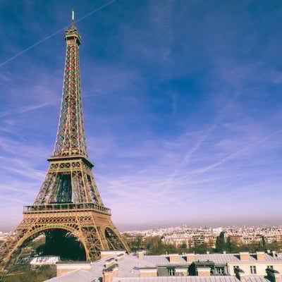 The Eiffel Tower framed against a vibrant blue sky streaked with aircraft contrails