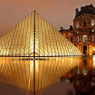 The illuminated glass pyramid of the Louvre glowing at night against the historic museum facade