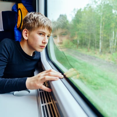 Young student gazing out the window of a moving train, reflecting the thoughtful planning that goes into choosing the right destination and theme for an educational tour.