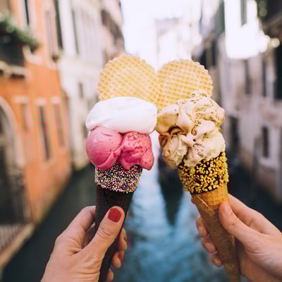 Two hands holding ice cream cones along a canal in Venice, illustrating the peace of mind that comes with Blue Dot’s included travel protection.