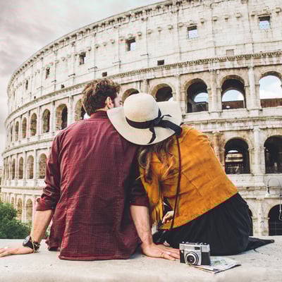 Traveler couple relaxing in front of the Colosseum in Rome, symbolizing how Blue Dot rewards help educators travel personally after a student tour.