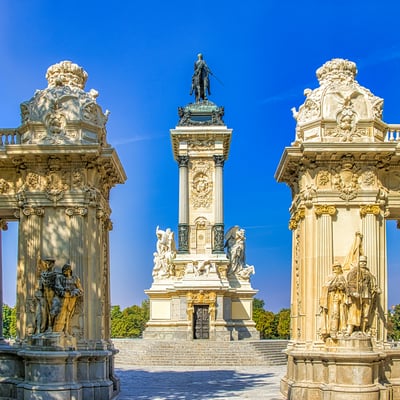 Monument to Alfonso XII towering over rowboats on the lake in Madrid’s El Retiro Park