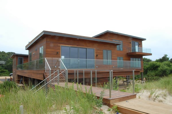 Raised wooden modular home beach house with glass sliding doors surrounded by beach sand and dune vegetation
