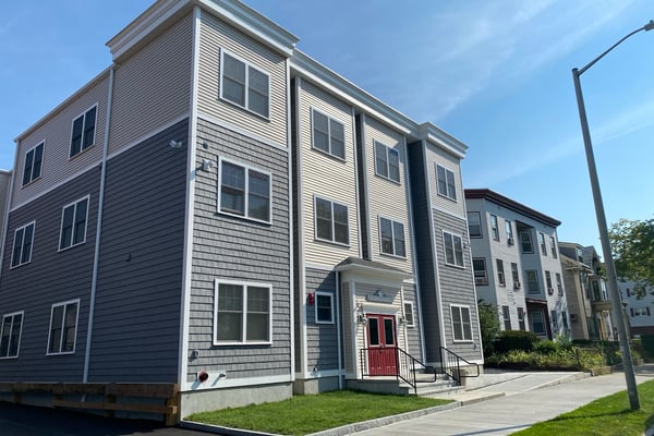 Gray three story multi-family building with steps leading to a red door